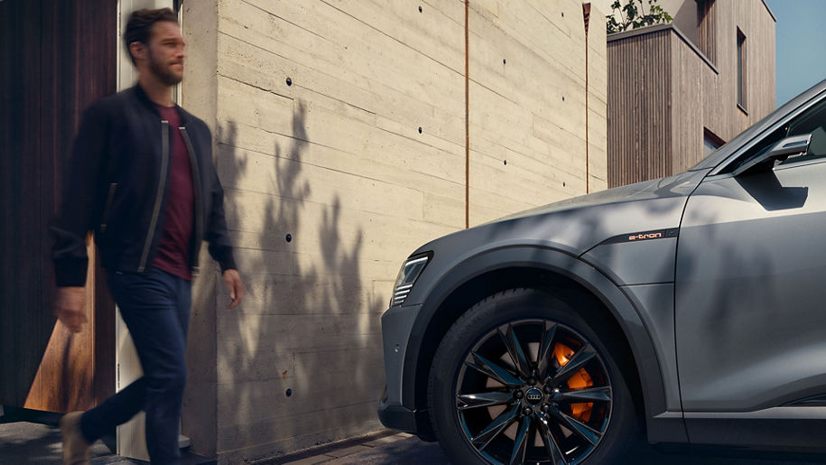 A man walking out of a wooden building towards his Audi e-tron.