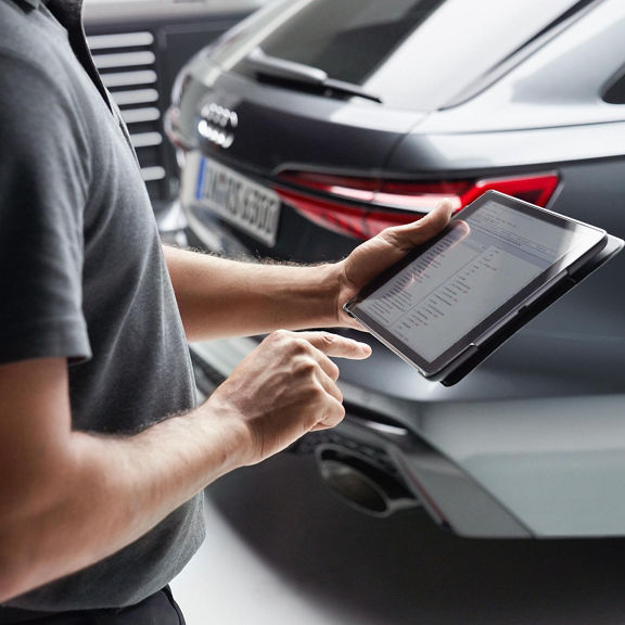 An Audi Service representative using a tablet computer. There is a blurred Audi in the background.