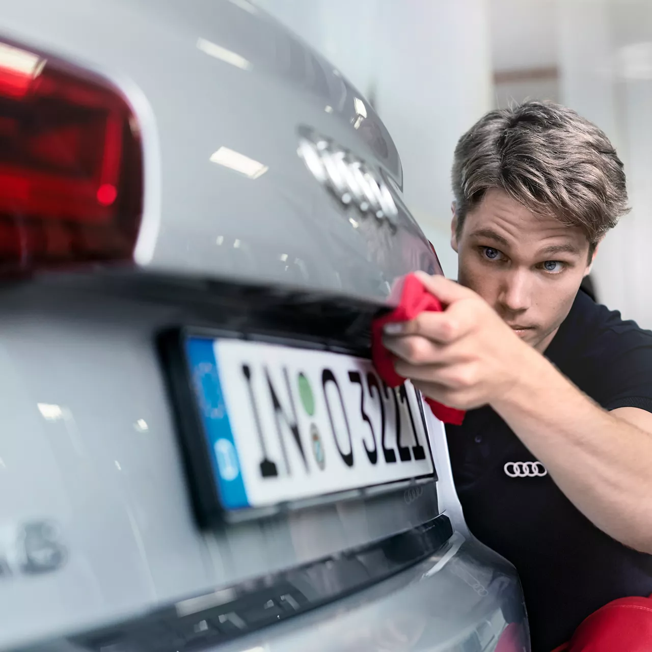 Närbild av en man som putsar bakdelen av en silvrig Audi Q3