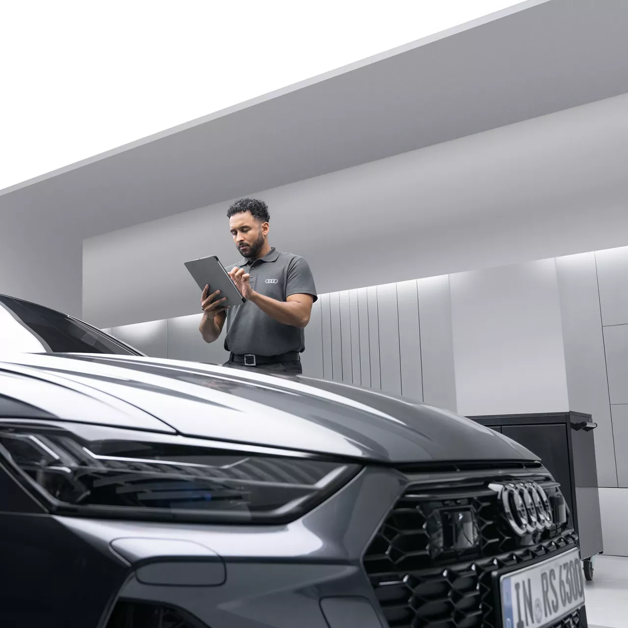 En av Audi servicepersonal som står bredvid och inspekterar en mörkgrå Audi RS