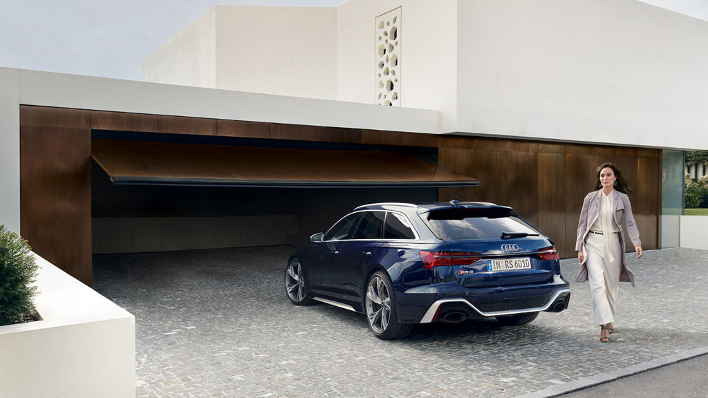 Audi RS6 bakifrån framför ett garage med en kvinna som går bredvid höger sida av bilen.