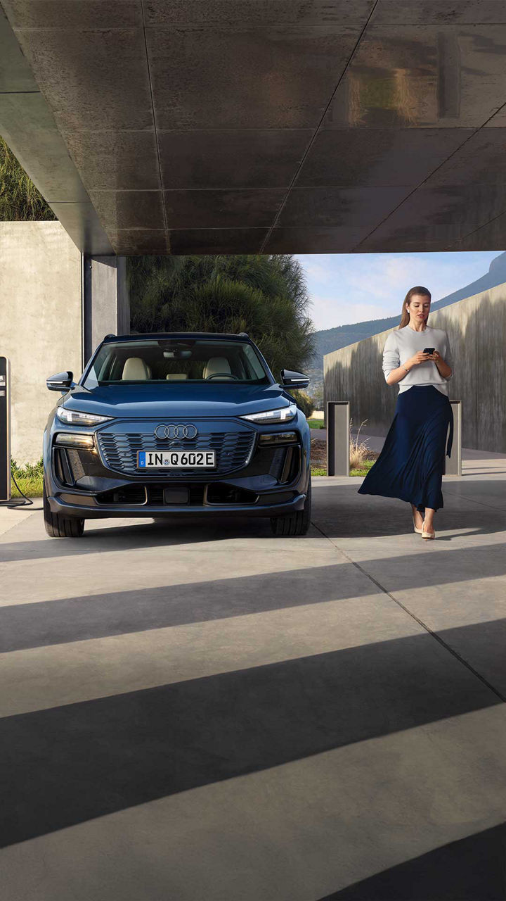 Audi Q6 e-tron aan de laadpaal, met een vrouw ernaast die op haar smartphone kijkt