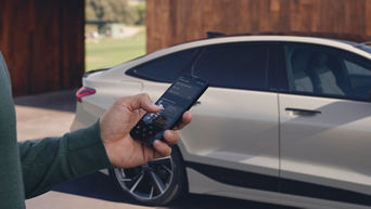 Une Audi A6 est garée devant une maison et la main d'un homme manipule son smartphone.