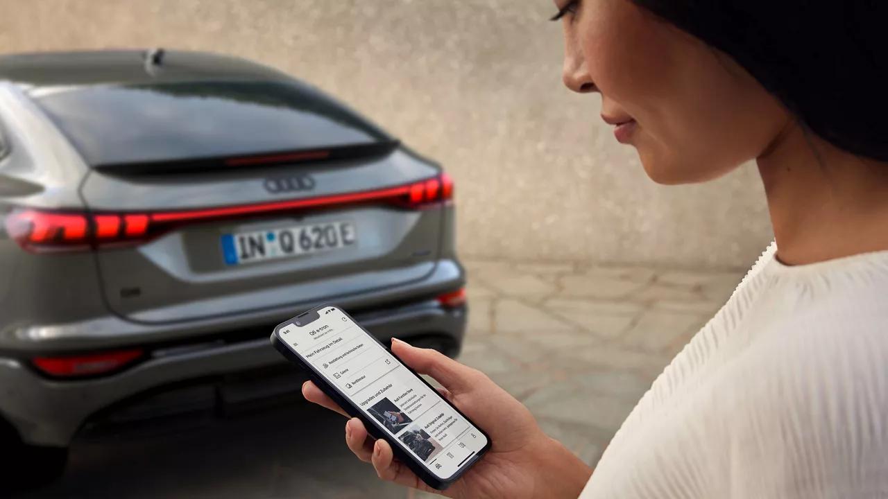 Audi Q6 Sportback im Hintergrund, davor eine Frau mit Handy
