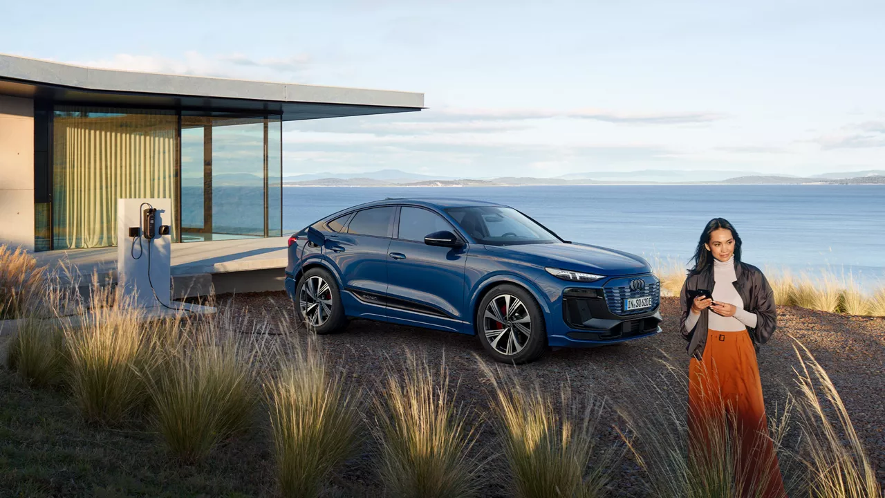 Eine Frau steht neben einem blauen Audi vor dem Meer