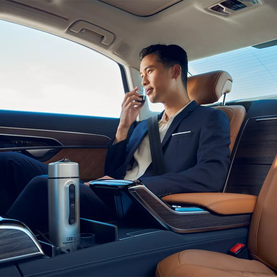 a man in the back seat sipping coffee made from an Audi mobile expresso machine