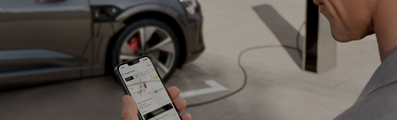 Person looking at their mobile phone with an Audi vehicle parked in the distance