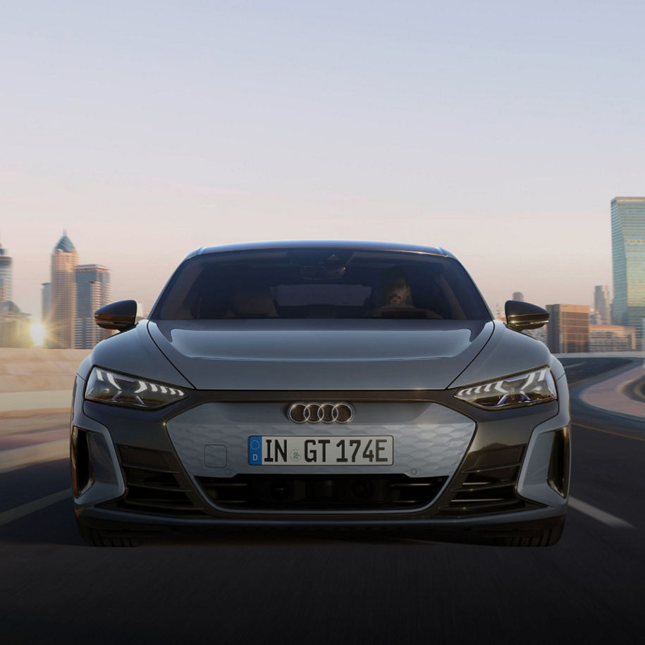 Silver Audi vehicle on road with city skyline in the background at sunrise