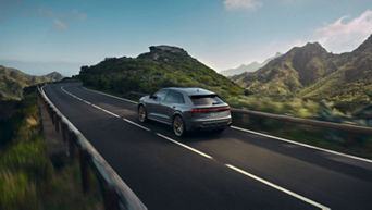 An Audi vehicle driving on a coastal road with mountains in the background