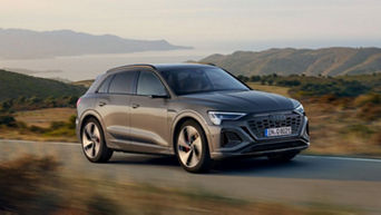  A grey audi vehicle driving on a coastal road with hills and the ocean in the background