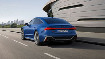 A blue Audi vehicle driving on a road with city skyline in the background