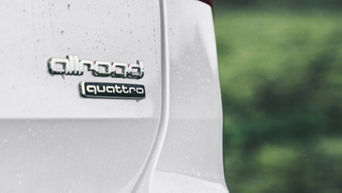  Close-up of an Audi vehicle's "allroad quattro" emblem on a wet white surface