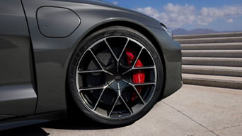 Close-up of an Audi vehicle's alloy wheel with red brake caliper and logo, parked by concrete steps