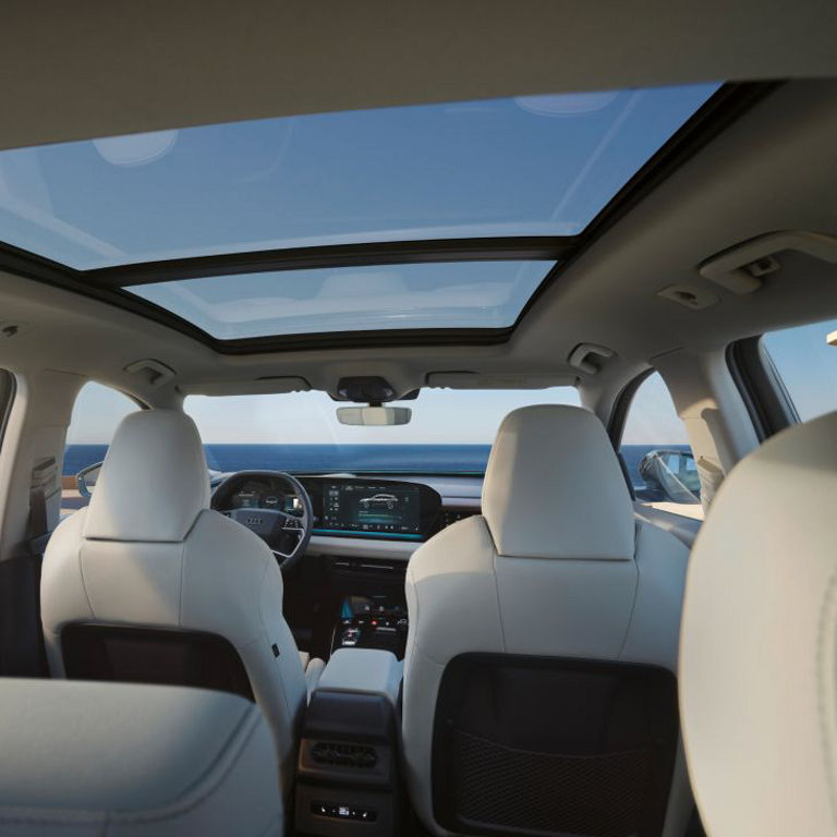 Interior view of an Audi vehicle with white seats, panoramic sunroof, and ocean view outside