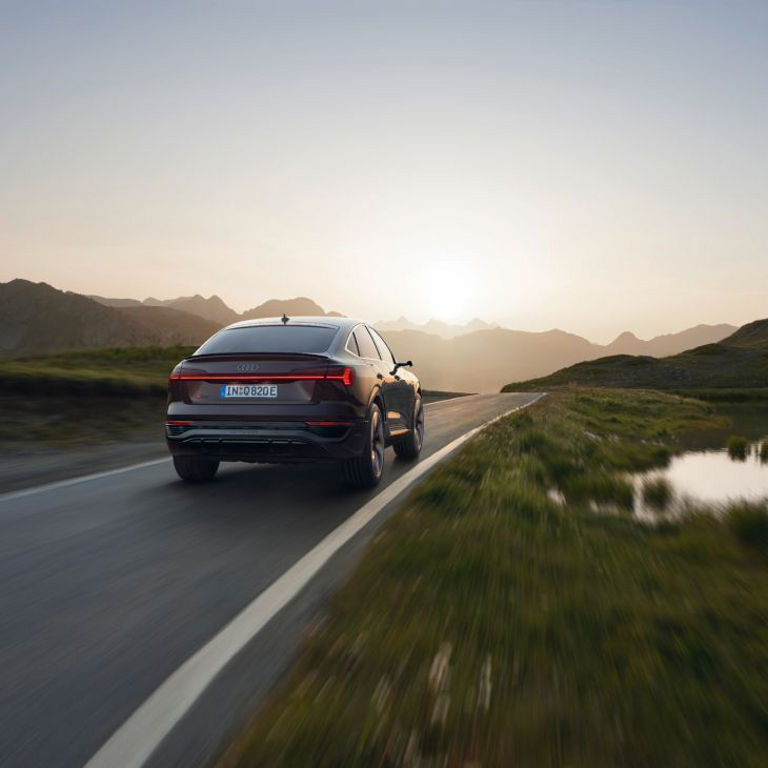 An Audi electric vehicle driving on a scenic mountain road at sunset