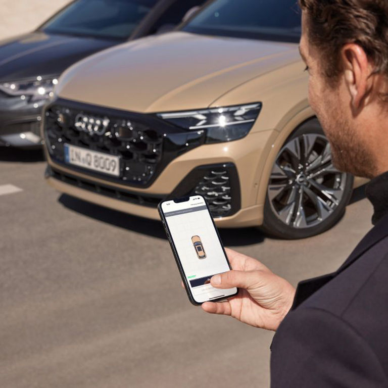 A person holding a smartphone with car control app before two parked Audi cars