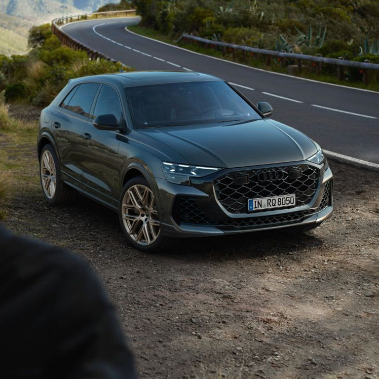 An Audi vehicle parked on a roadside with mountainous terrain in the background