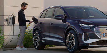 A man holding a charge cable and plugging it into the socket of a parked Audi electric vehicle