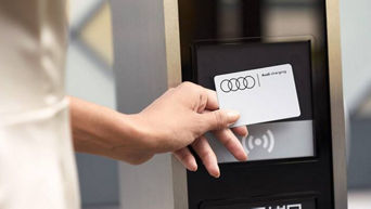 A woman's hand holding up an Audi Charging card at a charge station terminal