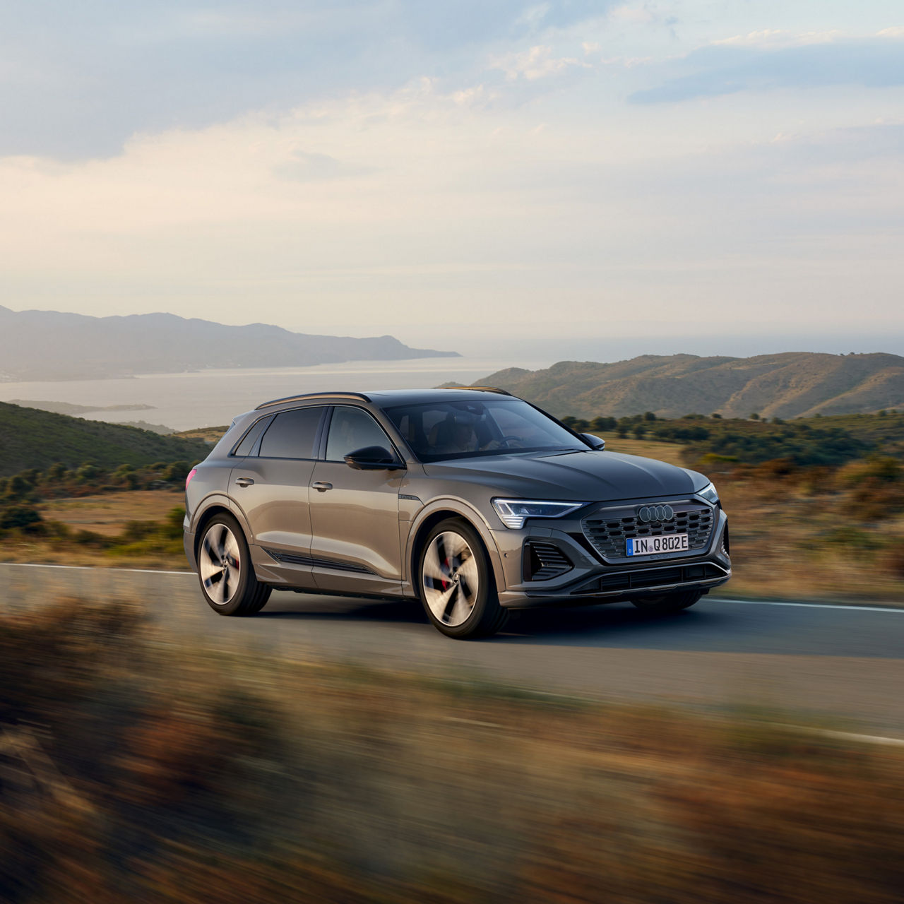 An Audi vehicle driving on a mountain road, water and mountains in the distance