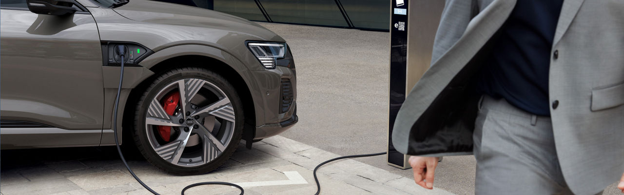 A man in a suit walking away from a parked Audi electric vehicle on charge at a charge station