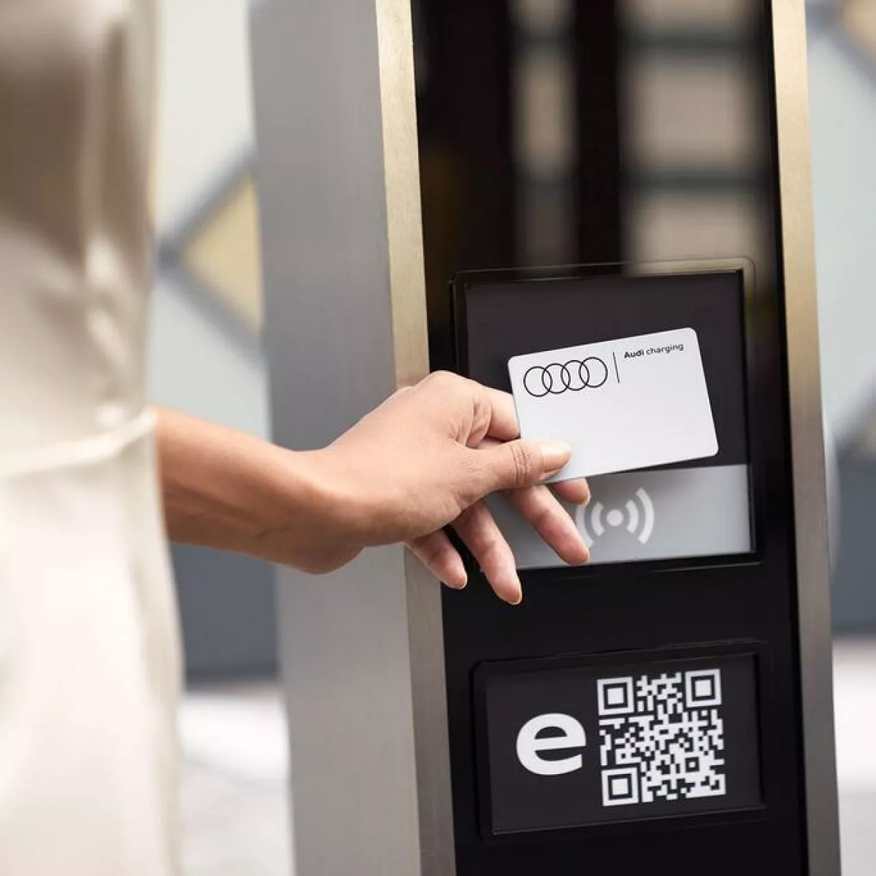 A woman's hand holding an Audi Charging card up to a charge station terminal