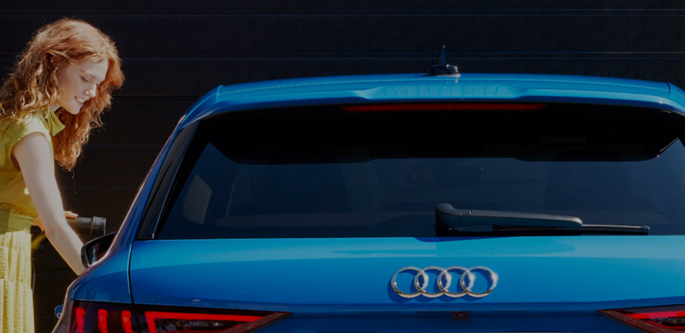 Young woman opening the door of a blue Audi ele