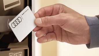 A hand holding an Audi Charging card up to a charge station terminal