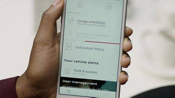 A hand holding up a mobile phone with the myAudi app visible on the display