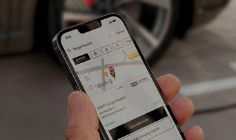 A hand holding a mobile phone with the myAudi app on screen