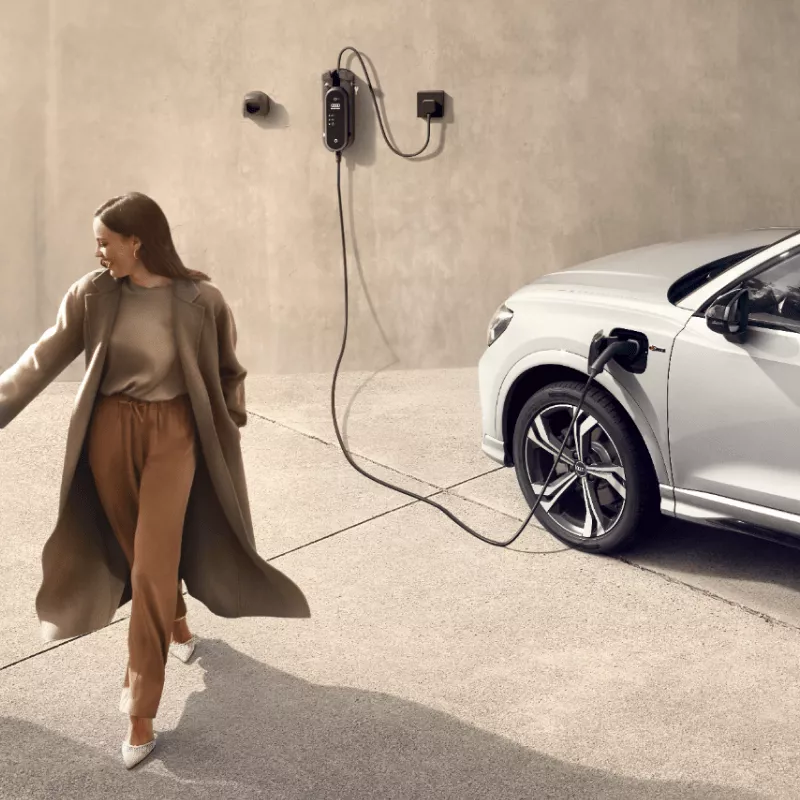 A young woman walking away from a white parked Audi electric vehicle on charge