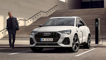 A white Audi electric SUV parked at a charging station outside a modern building.