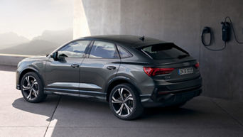 An Audi electric SUV parked and charging at a station with mountains in the background.