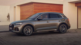 Silver SUV parked and charging at a station beside a building with wooden facade.