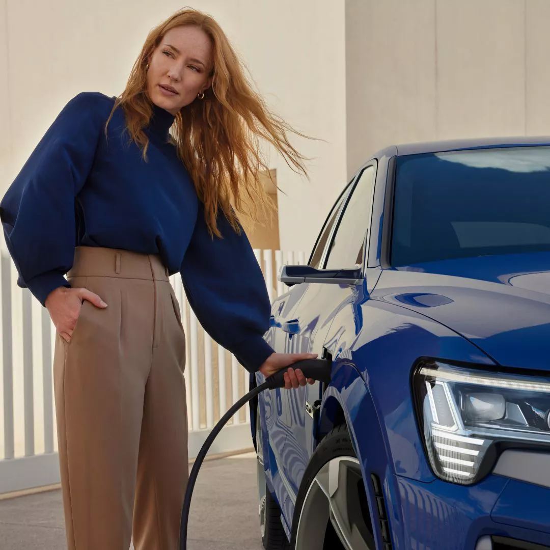  Young woman holding placing the charge cable into the charge port on a blue Audi electric vehicle