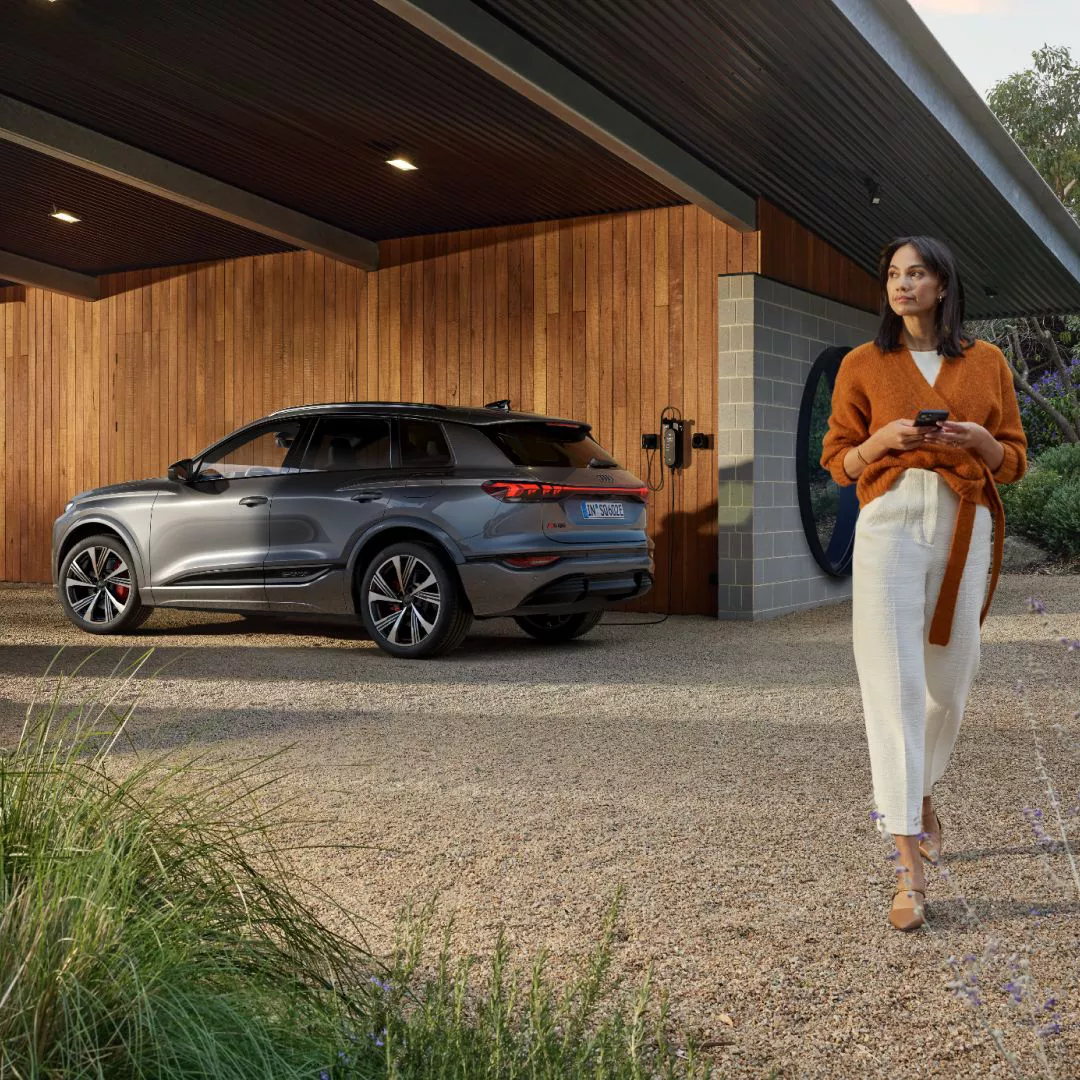  A woman walking away from an Audi vehicle connected to a charge point on a building in the distance