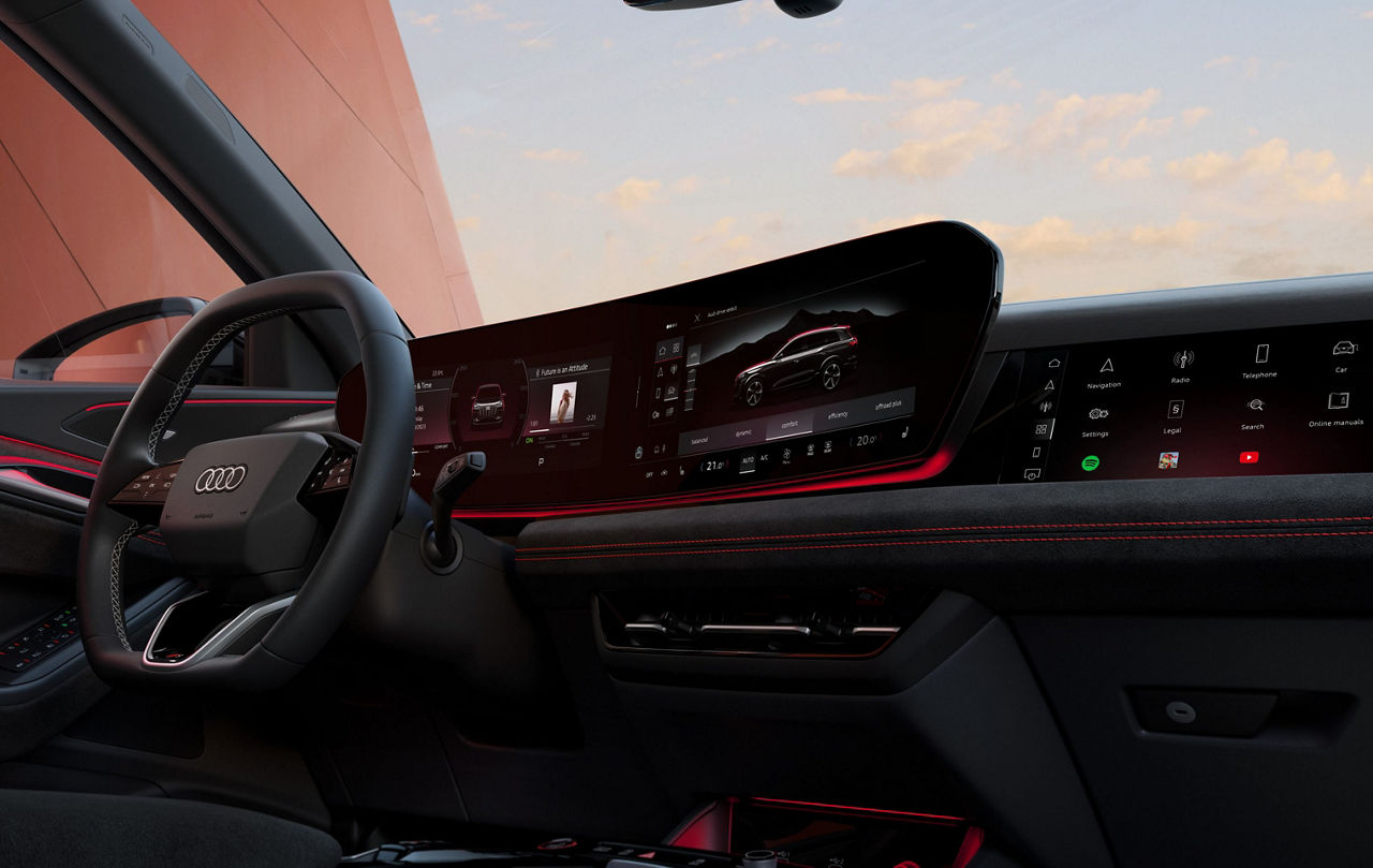 The interior of a Audi vehicle, steering wheel and dashboard illuminated with red lights in view