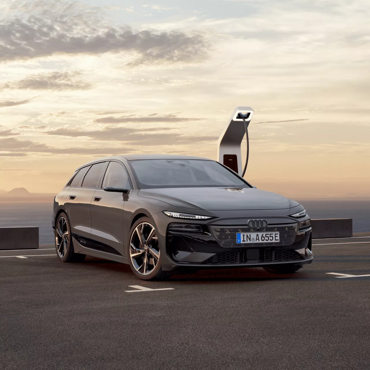 Grey Audi A6 Avant e-tron performance being charged outdoors, with a sunset background