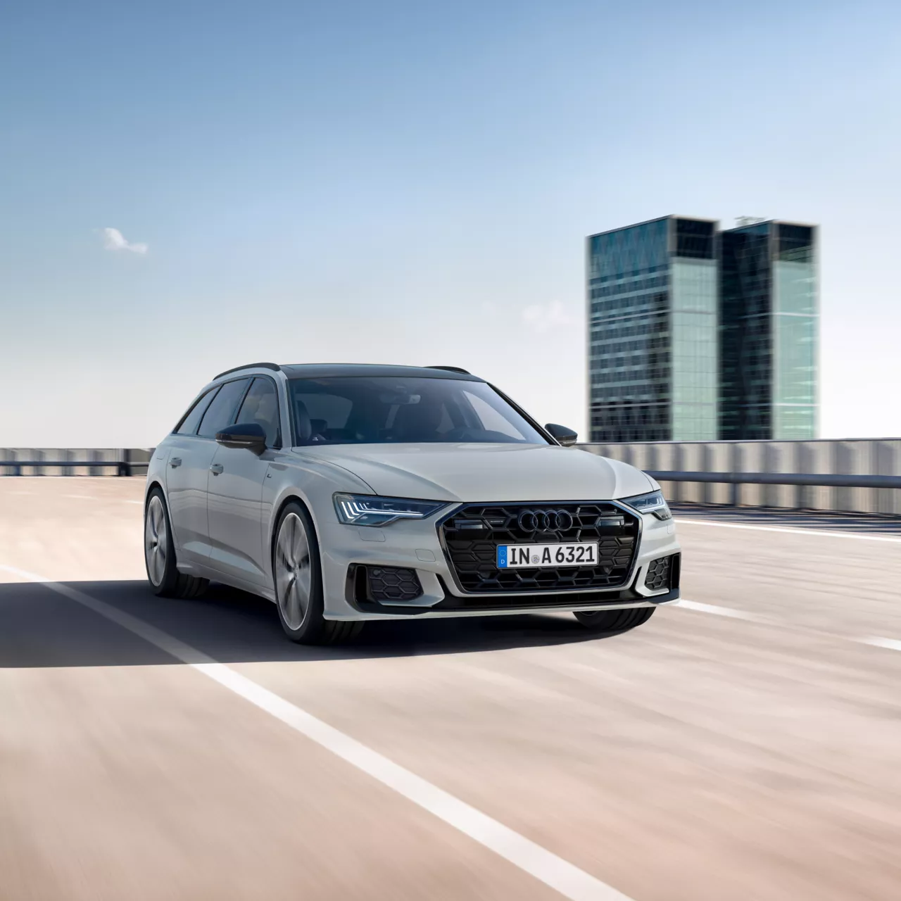 A light great Audi A6 Avant in action on the road, with a tall building featured on its right side