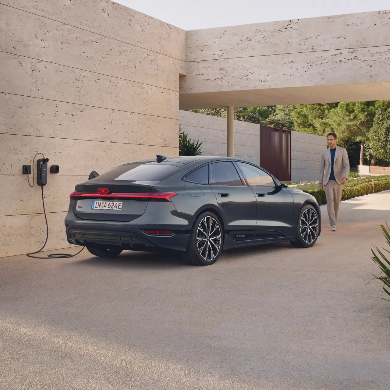 Dark grey Audi A6 Sportback e-tron performance being charged outside, with a man approaching the vehicle 