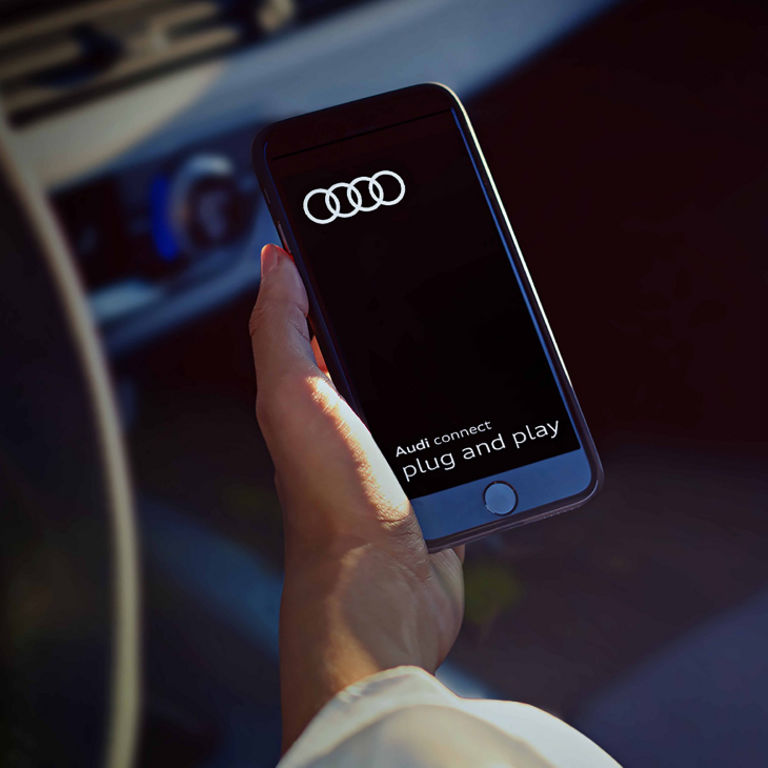 A mobile phone in a hand with the Audi Connect plug and play app displayed on screen