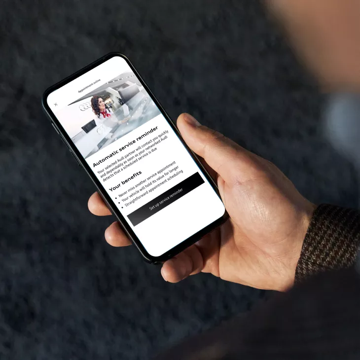 A mobile phone in a hand displaying the Audi Plug and Play app which is displaying an appointment