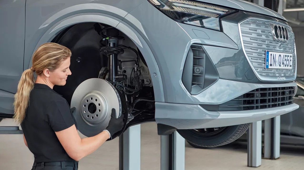 An Audi technician inspecting the front right wheel area of an Audi vehicle