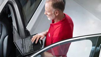 A mechanic holding a laptop beside an Audi that has the passenger door open