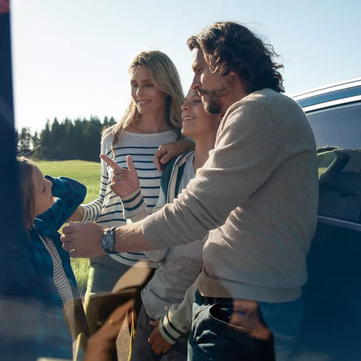 A young family of four all smiling beside a parked Audi vehicle