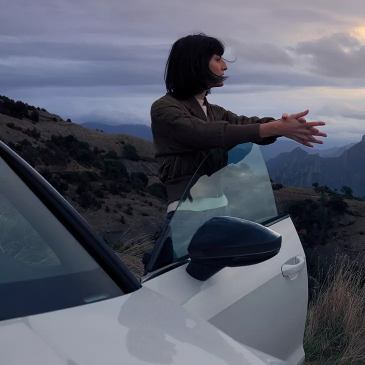 A woman leaning on the open door of a parked Audi vehicle in a hilly landscape