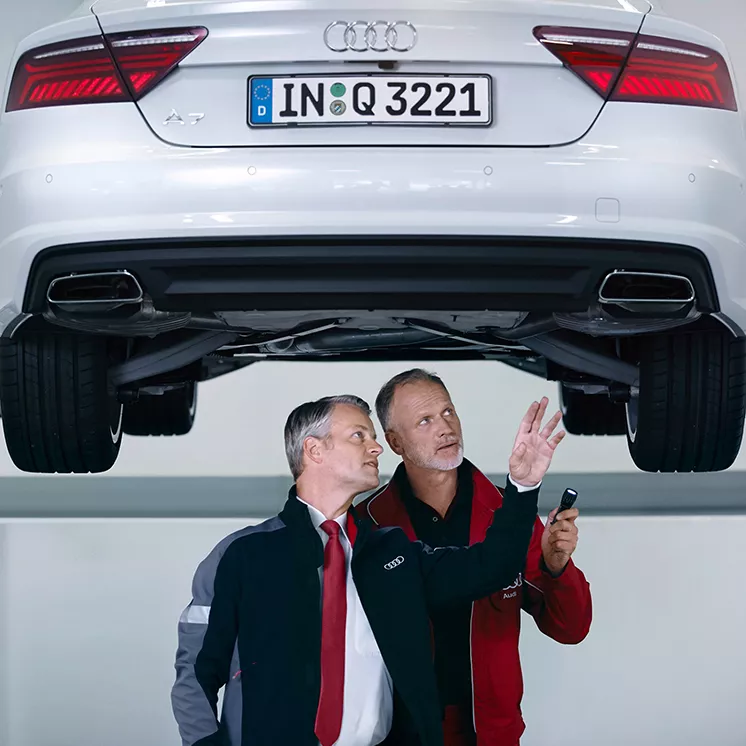 Two male Audi technicians inspecting the underside of an Audi vehicle.