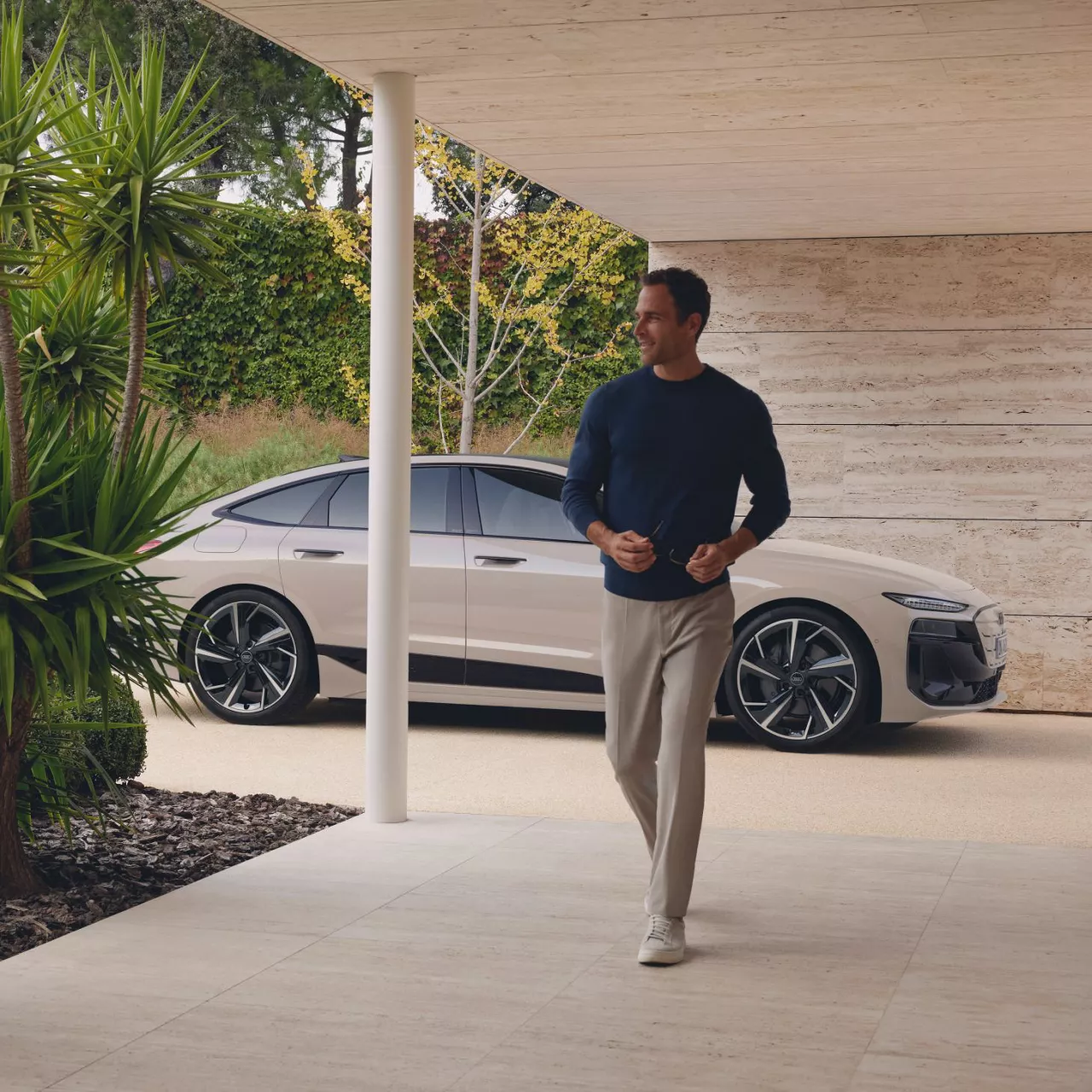 A man walking towards us, a parked Audi vehicle in the background