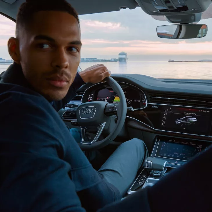 A male driver looking over his right shoulder, left hand on the steering wheel while reversing