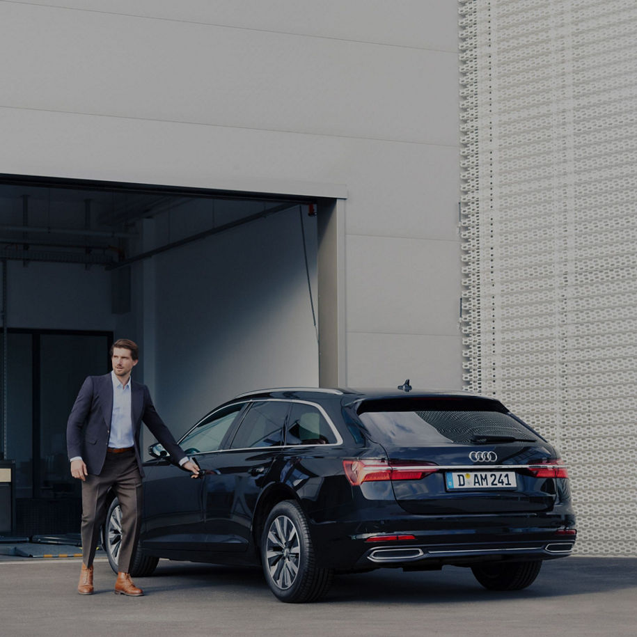 A suited man reaching out to the driver door hand on a parked Audi vehicle